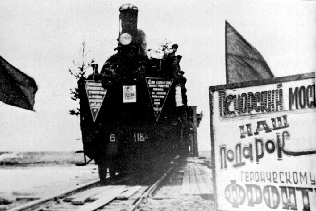 Открытие движения поездов по ледовой переправе через реку Печору. Надпись на плакате: «Печорский мост – наш подарок фронту».  1941 г.